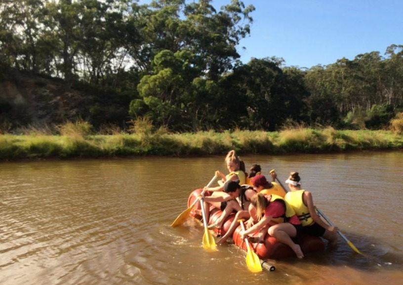 Students paddling a home-built raft across the dam