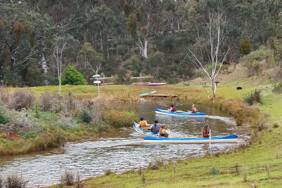 Canoes full of students crossing the dam surrounded by bushland