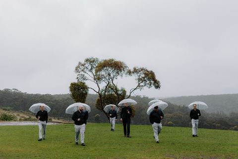 The bridal party walking across the paddock together under umbrellas in the rain