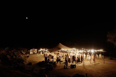 A marquee reception glowing with lights on the lawn at night