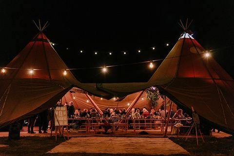 A tipi-style marquee lit up for the reception at night