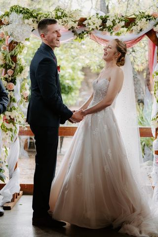 A couple holding hands and exchanging vows under a floral arch